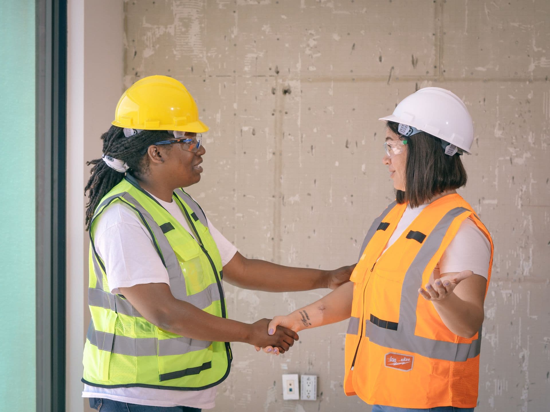 Two workers in hard hats and hi-vis vests shaking hands on site